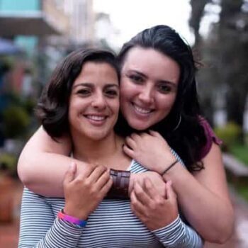 Portrait of beautiful female gay couple, partner hugging her from behind both smiling at camera very happy - LGBTQIA people